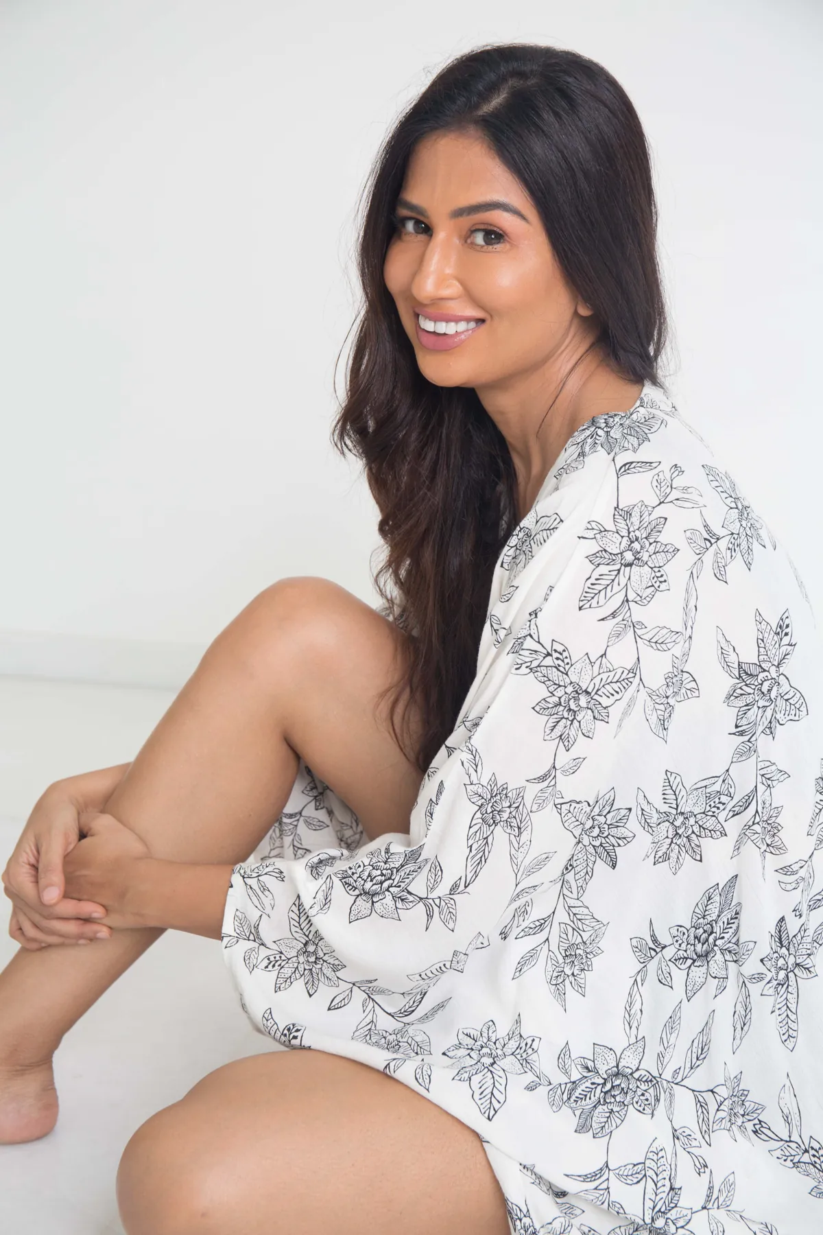 Uma Ghosh smiling over her shoulder in a white studio