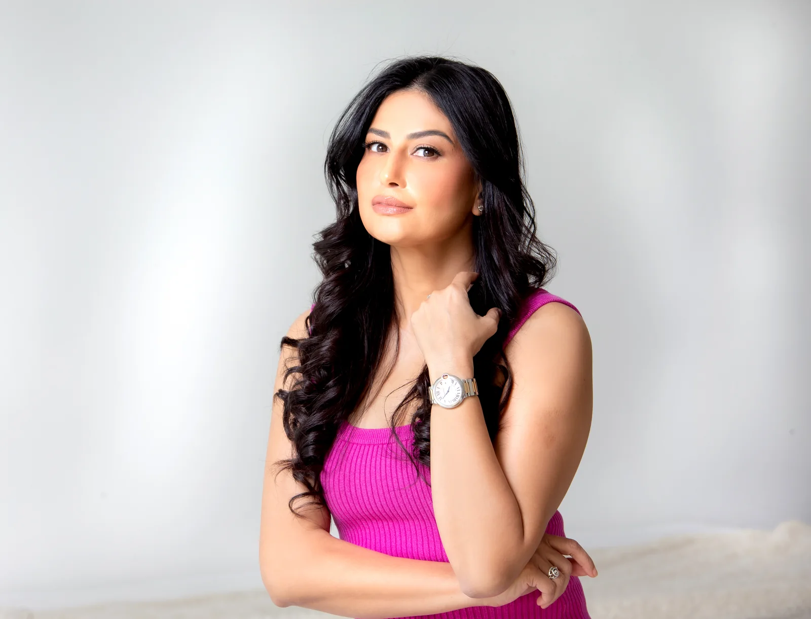 Uma Ghosh in a pink top, arms folded, against a soft white background