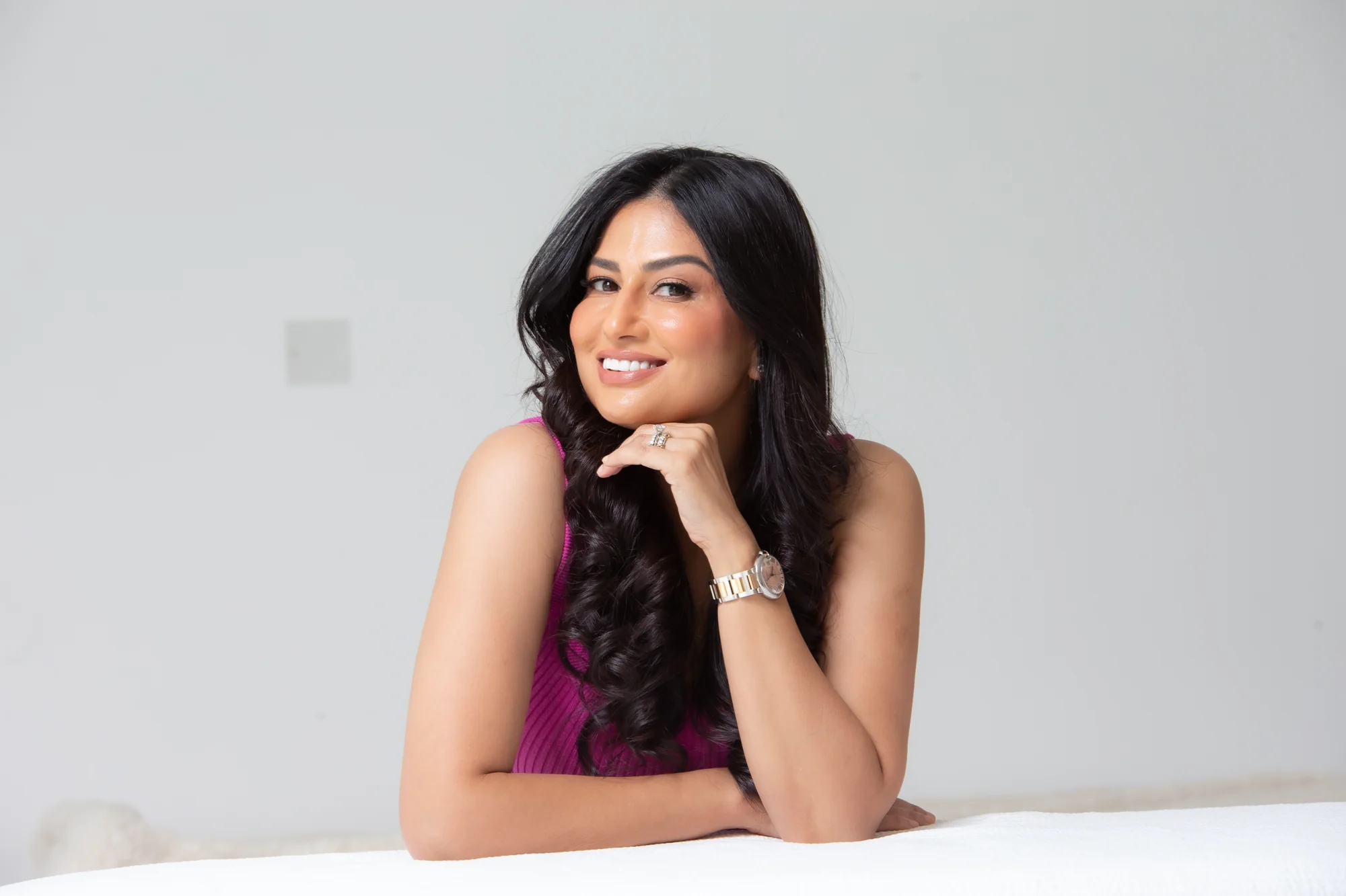 Uma smiling warmly with her chin resting on her hand